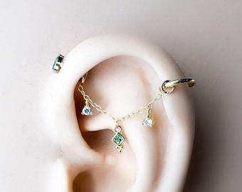 May include: Gold chain with small green and white gemstones hanging from a hoop earring. The chain is attached to a barbell piercing. The text "Chain Only" is visible at the bottom of the image.