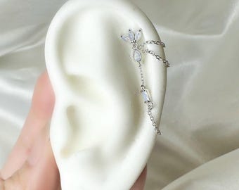 以下が含まれることがあります： 花柄クラスターデザイン、垂れ下がるチェーン、宝石のアクセントが特徴のシルバーイヤーカフ。 イヤーカフは耳の上部に着用するように設計されており、繊細でエレガントな外観です。 宝石は真珠光沢があります。