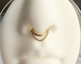 Könnte beinhalten: Goldener Nasenring mit einer Kette, die am Ring befestigt ist.