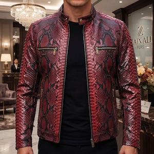 May include: A long-sleeve jacket featuring a red and black snakeskin pattern, a mandarin collar with a single snap button, a full-length front zip, and two horizontal zipped chest pockets. The jacket is worn over a plain black shirt.