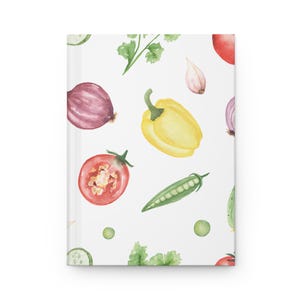 May include: A white hardback journal featuring a repeating watercolour pattern of fresh vegetables including red tomatoes, yellow bell peppers, purple onions, green peas in a pod, garlic cloves, and sprigs of green herbs scattered across the surface.