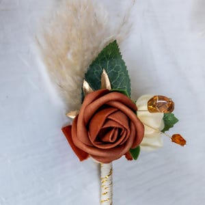 Boutonnière da sposa in stile boho con rosa in terracotta e dettagli in erba della pampa