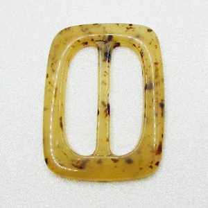 May include: A rectangular, double-bar buckle with rounded corners. The buckle is a translucent amber color with dark brown speckles throughout. The design features two oval openings separated by a central bar.