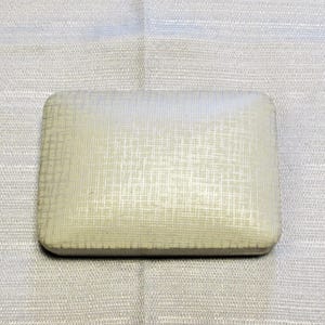 May include: A rectangular, off-white jewelry box with a subtle, grid-like woven texture across its surface. The box features rounded corners and a smooth, slightly domed lid, presenting a clean and uniform appearance for storage.