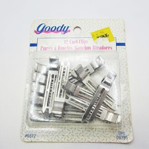 May include: A package of Goody brand 12 Curl Clips. The package is white and has a blue stripe with the Goody logo in pink. The clips are silver and are visible through the clear plastic packaging. The package has a yellow price tag.