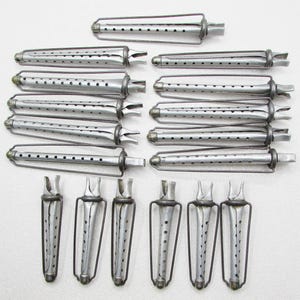 May include: An assortment of vintage silver-toned hair curlers. The curlers are cylindrical with small holes and a wire frame. Some have a unique, flared design at the end. The collection includes various sizes and styles, all made of metal.