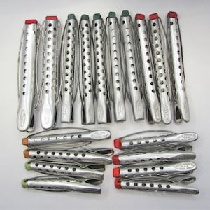 May include: A collection of vintage metal hair rollers with various colored end caps, including red, green, and orange. The rollers are silver-toned and have a perforated design. Some rollers are arranged vertically, while others are horizontal.