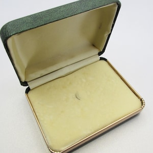 May include: Open vintage jewelry box with a green lid and a gold-colored trim. The interior is lined with a pale yellow fabric. The box is rectangular and appears to be made of a sturdy material.
