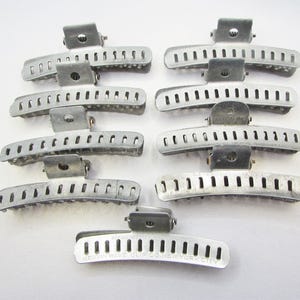 May include: A collection of eight vintage silver-toned metal hair clips. Each clip has a curved, slotted design with a hinged mechanism. The text "BERWIN WAVE CLIP CO. NEW YORK CITY" is visible on one clip. These clips are likely from the mid-20th century.