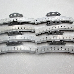 May include: Eight silver-toned hair barrettes with a curved design and the word "GOODY" stamped on each. The barrettes have a series of small, evenly spaced slots along their length and a central clasp.