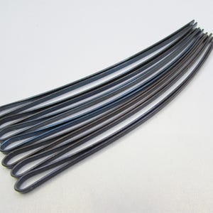 May include: A collection of dark gray bobby pins, arranged in a curved shape. The bobby pins are made of metal and have a smooth, slightly reflective surface. They are designed for securing hair in place.