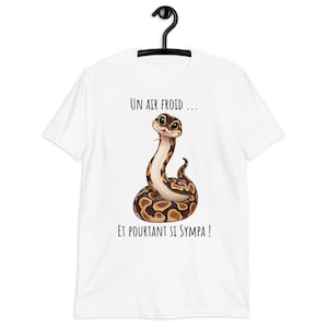 Könnte beinhalten: Ein weißes Kurzarm-T-Shirt mit einer Grafik einer braun-beigen gemusterten Schlange mit einer rosa Zunge. Über der Schlange steht der Text "UN AIR FROID ..." und unter der Schlange der Text "ET POURTANT SI SYMPA !" in schwarzer Schrift.