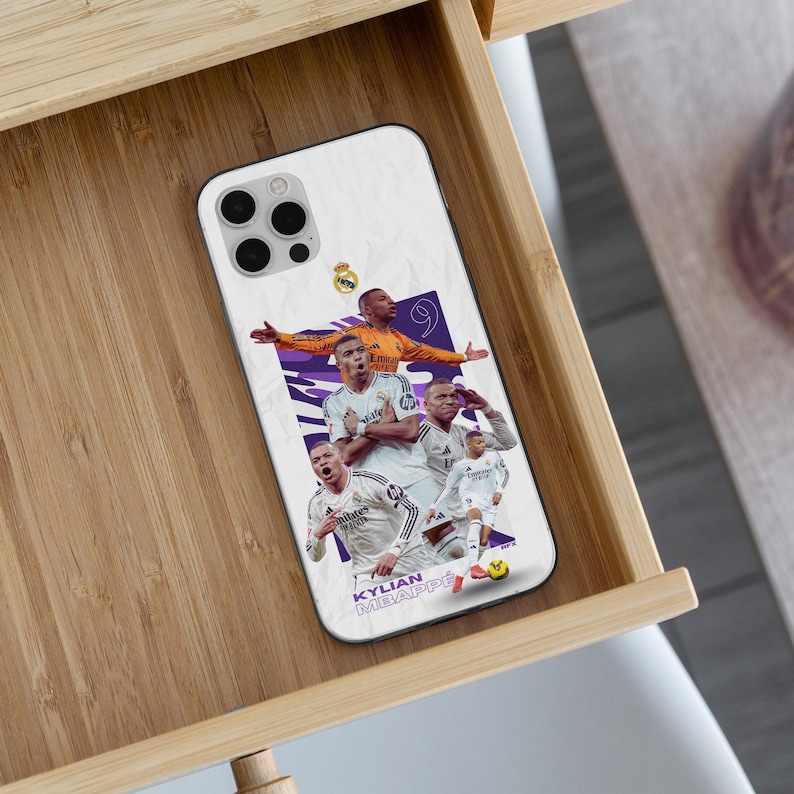 Puede incluir: Una funda de smartphone blanca con un collage de Kylian Mbapp&eacute; con equipaciones de f&uacute;tbol del Real Madrid. El dise&ntilde;o incluye al jugador en varias poses, el n&uacute;mero 9, el escudo del Real Madrid y el texto KYLIAN MBAPP&Eacute; en la parte inferior.