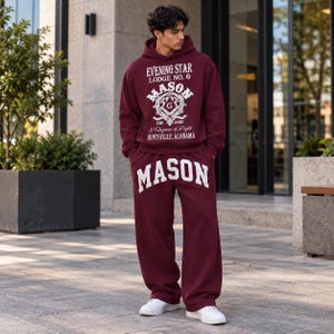 Pode incluir: Um conjunto de camisola com capuz e calças de fato de treino em cor bordeaux. A camisola apresenta o texto branco EVENING STAR LODGE NO. 6 MASON 281 ASKI 3 DEGREE OF LIGHT HUNTSVILLE, ALABAMA. As calças exibem a palavra MASON em letras brancas.