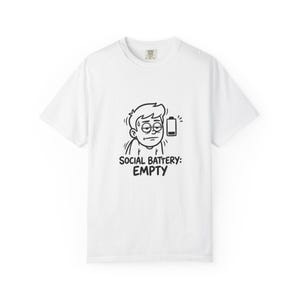 Pode incluir: Uma t-shirt branca de manga curta com um gráfico de linhas pretas de uma pessoa cansada com uma gota de suor e um ícone de bateria vazia. Abaixo da ilustração, o texto diz: SOCIAL BATTERY: EMPTY numa fonte preta e em negrito.