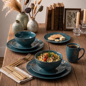 May include: A teal dinnerware set featuring a gold marble-like pattern, including bowls, plates, and a mug. The set is accompanied by gold-toned flatware, two ceramic vases with dried botanicals, three vintage books, and a framed botanical print.