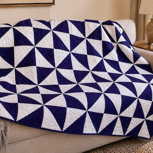 May include: A rectangular quilt featuring a repeating geometric pattern of dark navy blue and white triangles. The fabric surface displays a visible quilted texture with stitched lines forming the triangular shapes across the entire textile piece.