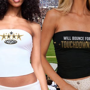 May include: A white strapless tube top featuring a gold star graphic with the text 1963 KNIGHTS and a black strapless tube top with the text WILL BOUNCE FOR TOUCHDOWNS in gold lettering. Both tops are fitted and designed for a sleek, athletic appearance.