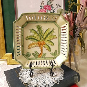 May include: A square ceramic bowl with a cream-colored base, featuring a central illustration of a green palm tree with brown coconuts. The bowl has a decorative lattice-style rim with green trim and a bamboo-patterned border around the center.