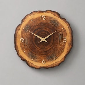 May include: A round wall clock crafted from a natural wood slice featuring a dark brown centre with visible grain rings and a lighter outer edge. The clock face includes gold-coloured metal hands and gold numerals at 12, 3, 6, and 9.