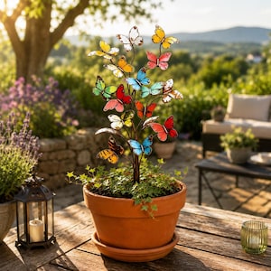 Könnte beinhalten: Ein Terrakottatopf mit einer Metallskulptur in Baumform, die mit zahlreichen bunten Schmetterlingsornamenten in Rot, Gelb, Blau, Orange und Grün verziert ist. Die Schmetterlinge sind an dünnen Metallzweigen befestigt und bilden ein Dekor.