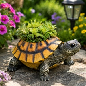 Könnte beinhalten: Ein schildkrötenförmiger Pflanzkübel mit strukturiertem grauem Kopf und Gliedmaßen sowie einem leuchtend gelben, schwarz gemusterten Panzer, der eine Ansammlung kleiner grüner Sukkulenten enthält. Die Skulptur steht auf einer Steinplatte.