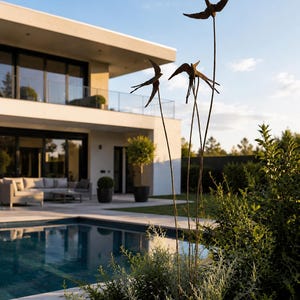Könnte beinhalten: Eine Metall-Gartenskulptur mit drei dunkelbraunen Vogelsilhouetten, die auf dünnen, hohen Stäben montiert sind. Die Vögel sind im Flug dargestellt und in unterschiedlichen Höhen positioniert, was eine vertikale Anordnung ergibt.