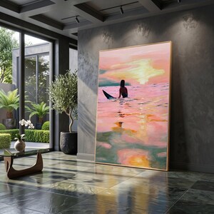 Puede incluir: Una pintura rectangular grande en un marco de madera fino que representa a una persona en una tabla de surf en el océano al atardecer. La escena presenta tonos vibrantes de rosa, naranja y amarillo que se reflejan en la superficie del agua.
