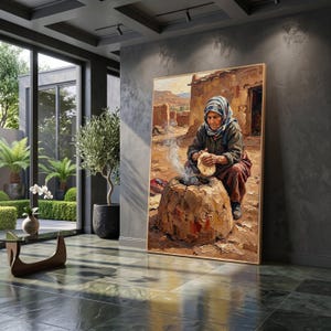 May include: A framed oil painting depicting an elderly person wearing a headscarf and dark clothing, kneeling on the ground while preparing flatbread over a traditional clay oven with visible smoke rising in a desert-like outdoor setting.