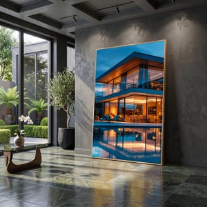 May include: A large rectangular wall art piece featuring a modern two-story house with floor-to-ceiling glass windows, warm interior lighting, and a swimming pool reflecting the structure at dusk, all framed in a thin gold-toned metal border.
