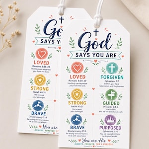 May include: Two white rectangular paper tags with rounded top corners and white string loops. The text reads God Says You Are, followed by six colorful icons representing Loved, Forgiven, Strong, Guided, Brave, and Purposed, with Bible verses.