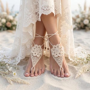 May include: Cream-colored crochet barefoot sandals featuring a central floral motif and a triangular lattice pattern. The design includes thin, adjustable ties that wrap around the ankles, accented with small wooden beads at the ends of the strings.