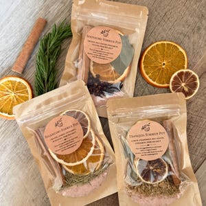 May include: Three clear pouches containing simmer pot ingredients labeled Soothing, Balancing, and Tranquil. Each pouch holds dried orange slices, cinnamon sticks, herbs, and pink sea salt. Loose dried orange slices and rosemary sprigs are nearby.