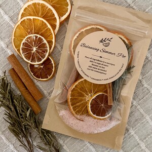 May include: A clear plastic pouch containing a Balancing Simmer Pot kit with dried orange and lemon slices, cinnamon sticks, rosemary, and pink Himalayan sea salt. The label includes instructions to simmer in water, noting it is not for consumption.