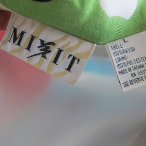 May include: A white, blue, and pink rayon jacket with a "MIXIT" label and a size L tag. The tag lists the fabric composition as 100% rayon for the shell and 100% polyester for the lining. It also states that the jacket was made in Taiwan and includes the RN number 11935. The tag instructs the user to see the reverse side for care instructions.
