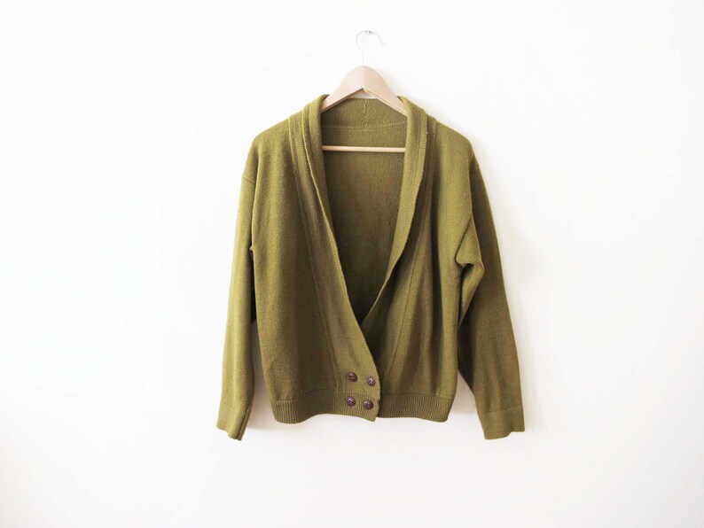Puede incluir: Un c&aacute;rdigan verde con cuello chal y dos botones. El c&aacute;rdigan est&aacute; hecho de una tela suave y de punto.