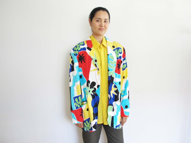 May include: A colorful abstract print blazer with a yellow button-down shirt underneath. The blazer has a white background with red, blue, green, and black abstract shapes.