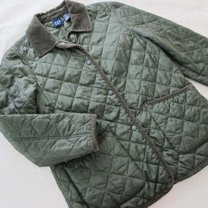 May include: An olive green quilted jacket featuring a diamond-patterned stitch, a dark brown corduroy collar, and matching corduroy trim along the front placket and cuffs. The jacket includes a front snap-button closure and two large patch pockets.