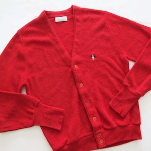 May include: A bright red cardigan sweater with a V-neck and button-up closure. The sweater features long sleeves with ribbed cuffs and a small penguin logo on the chest. The sweater is made of a soft, textured material.