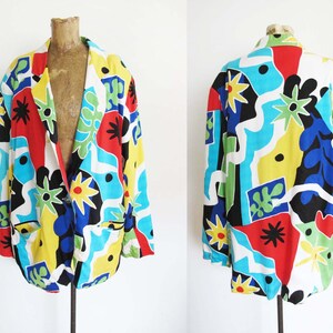 May include: A colorful blazer with a geometric abstract print in shades of red, blue, yellow, green, and black. The blazer has a white background and a button closure.