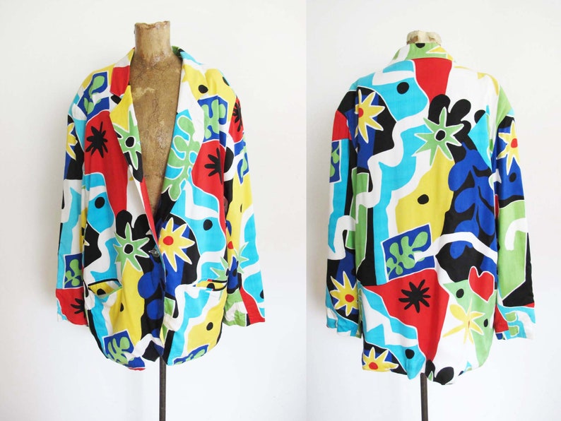 May include: A colorful blazer with a geometric abstract print in shades of red, blue, yellow, green, and black. The blazer has a white background and a button closure.