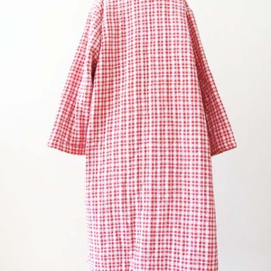 May include: A red and white gingham patterned coat with long sleeves. The coat is quilted and has a collar.