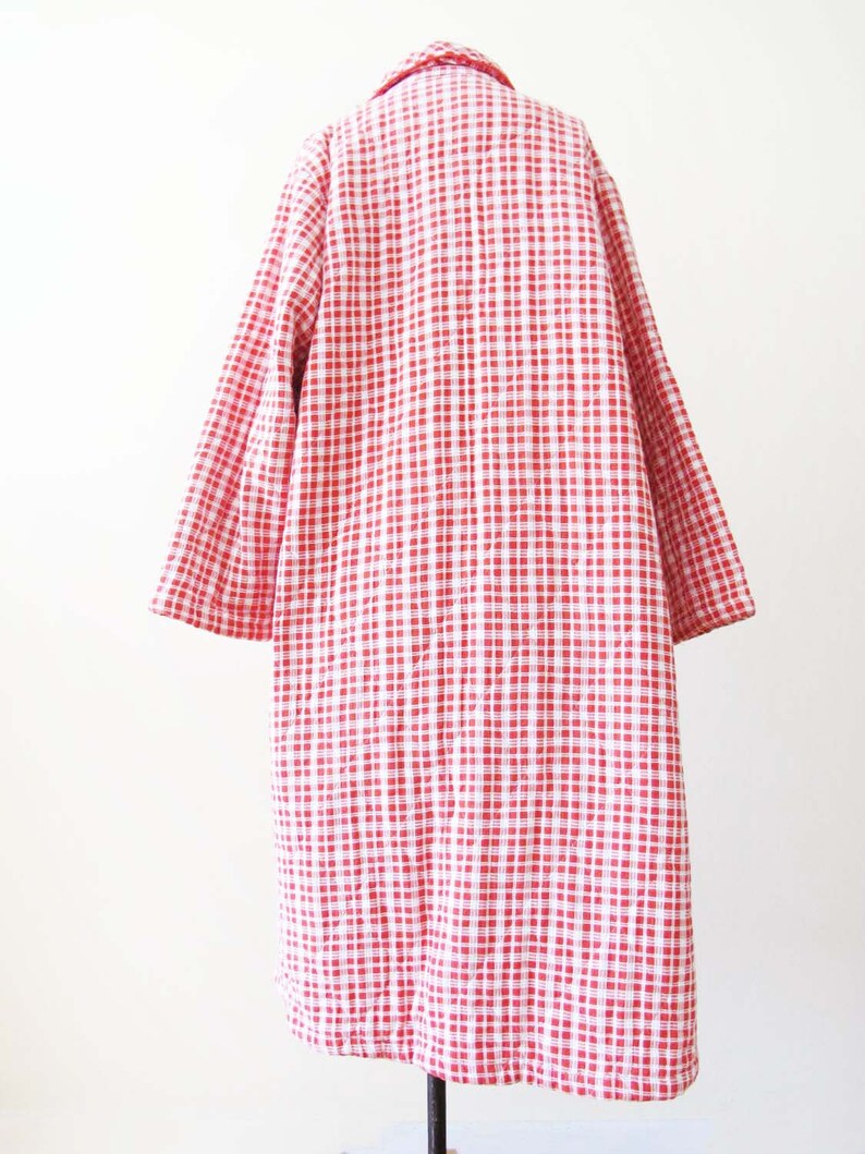May include: A red and white gingham patterned coat with long sleeves. The coat is quilted and has a collar.