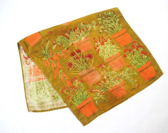 May include: A brown linen tea towel with a colorful pattern of potted plants and flowers. The plants are labeled with their names, such as "Thyme" and "Rosemary".
