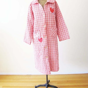 May include: A red and white gingham robe with a long sleeve and button closure. The robe has red heart appliques on the front and pockets.