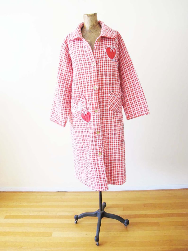 May include: A red and white gingham robe with a long sleeve and button closure. The robe has red heart appliques on the front and pockets.