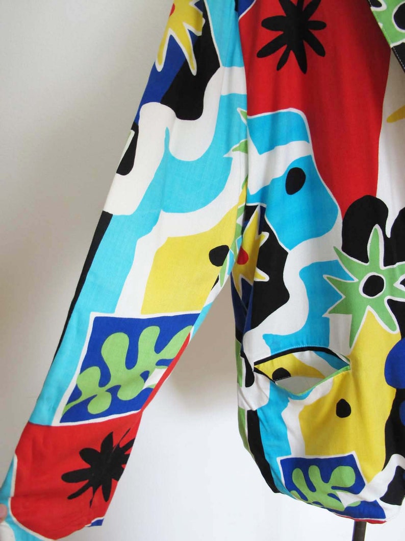 May include: A colorful, abstract patterned jacket with a long sleeve. The jacket is made of a lightweight fabric and features a variety of colors, including red, blue, yellow, green, and black.