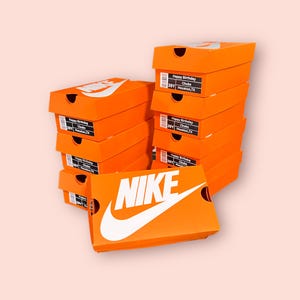 以下が含まれることがあります： 鮮やかなオレンジ色のNikeの靴箱が積み重なっており、白いロゴが描かれています。各箱には、Happy Birthday、Chubs、39Y、Houston, TXという文字が書かれた白黒のラベルが貼られています。箱は2列に並べられ、手前に1つの箱が水平に置かれています。