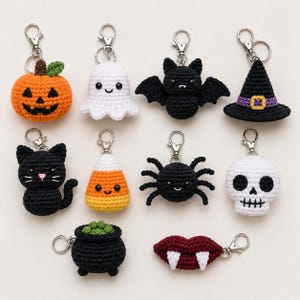 May include: A collection of ten crocheted Halloween-themed keychains featuring an orange pumpkin, white ghost, black bat, black witch hat, black cat, candy corn, black spider, white skull, black cauldron with green contents, and red lips with fangs.