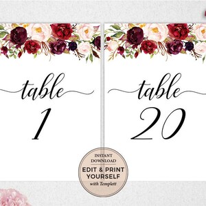 May include: Two white table number cards with burgundy floral designs. The text "table" is written in a script font with the numbers "1" and "20" below. The text "Instant Download Edit & Print Yourself with Templett" is printed on a circle in the bottom right corner of the card.